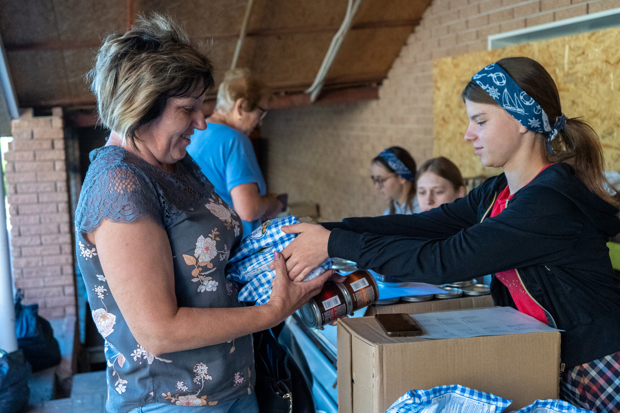A young woman hands another woman food supplies across a table